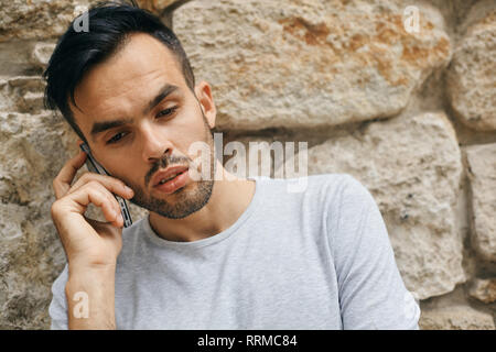 Portrait of handsome male student outdoors on university campus and talking on mobile phone, copy space. Confident and successful student. Education,  Stock Photo