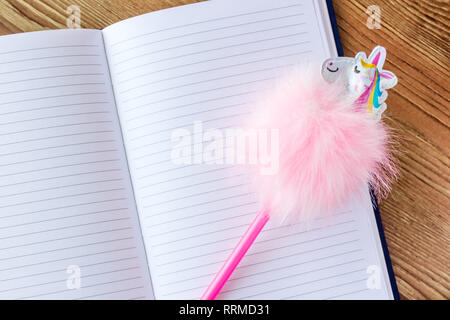 Funny unicorn pen on lined blank notebook on wooden table. Stock Photo