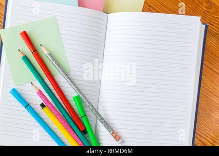 Colorful pencils and felt-tip pens on opened lined notebook. Stock Photo