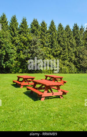 Rest area with red picnic tables on green lawn in a park. Stock Photo
