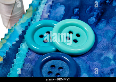 Multi-colored remnants of fabric with large buttons and a spool of thread with shallow depth of field  isolated on white Stock Photo