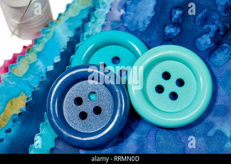 Multi-colored remnants of fabric with large buttons and a spool of thread with shallow depth of field  isolated on white Stock Photo