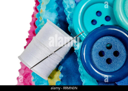 Multi-colored remnants of fabric with large buttons and a spool of thread with shallow depth of field  isolated on white Stock Photo