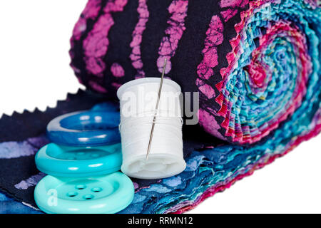 Multi-colored remnants of fabric with large buttons and a spool of thread with shallow depth of field  isolated on white Stock Photo