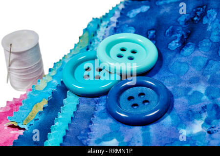 Multi-colored remnants of fabric with large buttons and a spool of thread with shallow depth of field  isolated on white Stock Photo