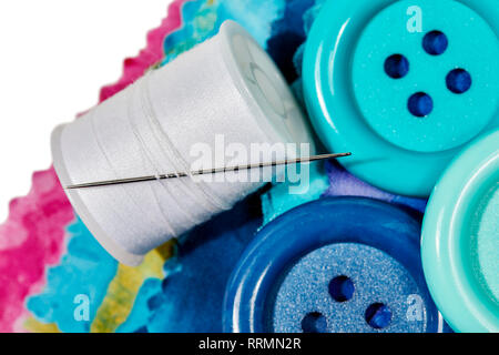 Multi-colored remnants of fabric with large buttons and a spool of thread  with a needle in it with shallow depth of field  isolated on white Stock Photo
