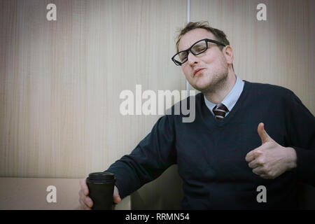 A man at work giving a thumbs up while drinking his coffee. Stock Photo