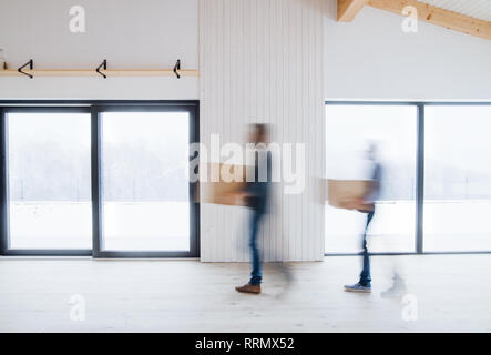 Unrecognizable men walking with cardboard boxes when furnishing new house. Intentional motion blur. Stock Photo