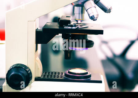 side view of a a light microscope with knobs and screws with light on Stock Photo