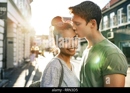 Young man kissing his smiling girlfriend on a city street Stock Photo