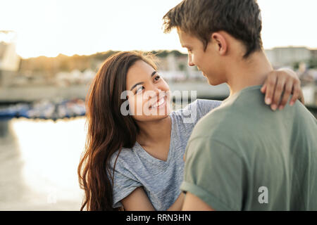 Affectionate young couple smiling while standing outside by a harbor Stock Photo