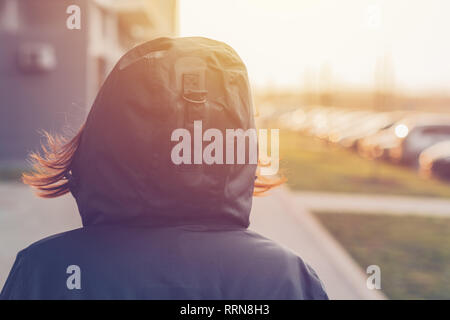 Rear view of hooded female person walking the city street in cold winter afternoon Stock Photo