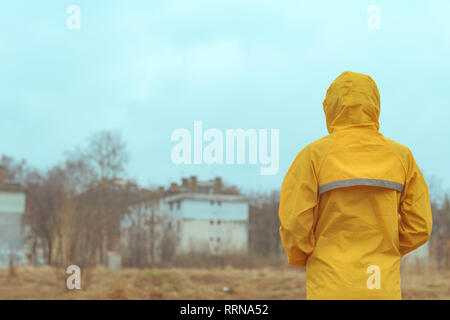 Rear view of woman in raincoat looking into distance on cloudy rainy winter day Stock Photo