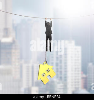 Businessman shackled by gold house hanging on the rope, on city buildings background. Stock Photo