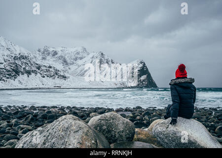 Woman in warm clothing enjoying remote snowy ocean and mountain view, Lofoten Islands, Norway Stock Photo