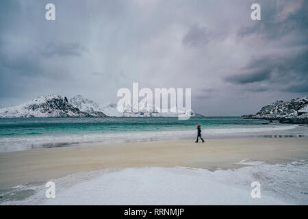 Woman walking on cold, snowy beach, Lofoten Islands, Norway Stock Photo