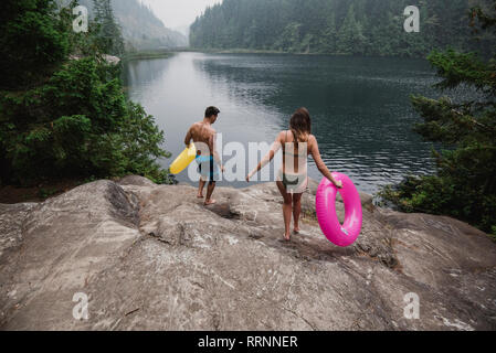Young couple with inflatable rings at remote lakeside, Squamish, British Columbia, Canada Stock Photo