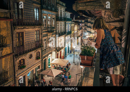 Woman standing on balcony, looking at ornate architecture, Porto, Portugal Stock Photo