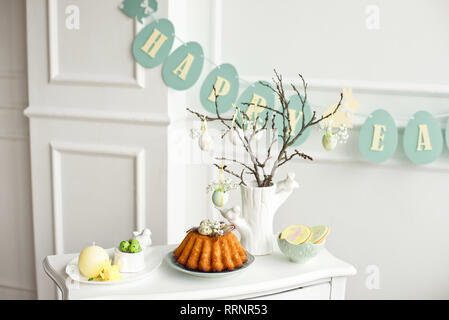 Decoration of the Easter table, a vase with a branch and decorations from flowers and eggs, biscuits with rabbit, Easter cake and sweets Stock Photo