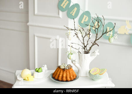 Decoration of the Easter table, a vase with a branch and decorations from flowers and eggs, biscuits with rabbit, Easter cake and sweets Stock Photo