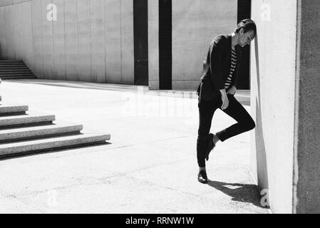 Young man leaning against sunny urban wall Stock Photo