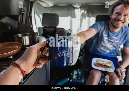 Personal perspective couple toasting coffee cups in camper van Stock Photo