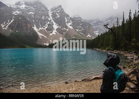 Serene hiker in rain jacket enjoying tranquil mountain and lake view, Banff, Alberta, Canada Stock Photo
