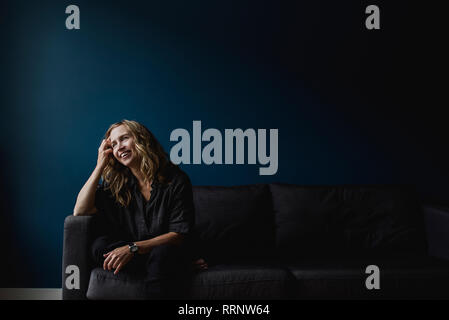 Happy woman sitting on sofa, looking away Stock Photo