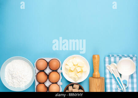Ingredients for baking or cooking on blue background. Eggs, butter, flour, measuring spoons and rolling pin. Pin up or retro style kitchen food backgr Stock Photo