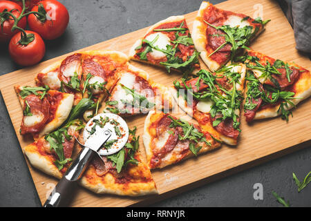 Pizza or flatbread with arugula, salami, cheese sliced on wooden cutting pizza board Stock Photo