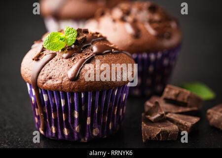 Tasty chocolate muffins closeup view. Chocolate cakes or cupcakes with ganache and mint leaf Stock Photo