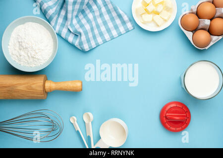 Baking ingredients on blue background. Rolling pin, flour, eggs, butter, measuring spoons and other cooking baking ingredients for cake, pastry or coo Stock Photo