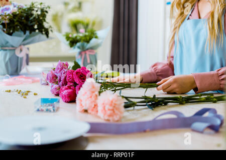 cropped view of female florist sitting at table with pink roses and carnations while arranging bouquet Stock Photo