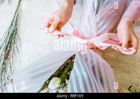 partial view of female florist tying bow with ribbon while wrapping flower bouquet Stock Photo