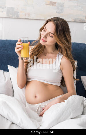 Carefree pregnant woman drinking juice in bed Stock Photo