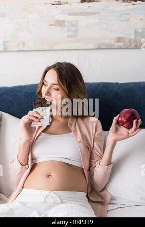 Pregnant woman holding apple and eatng chocolate Stock Photo