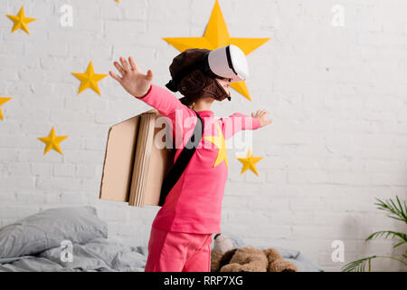 Kid in vr headset and pink clothes waving hands in bedroom Stock Photo