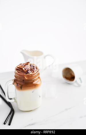 Ice coffee with milk in mason jar and black metal drinking straws on white marble table over white background. Copy space for text. Stock Photo