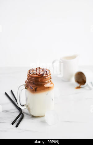 Ice coffee with milk in mason jar and black metal drinking straws on white marble table over white background. Copy space for text. Stock Photo
