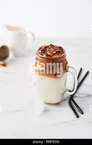 Ice coffee with milk in mason jar and black metal drinking straws on white marble table over white background. Copy space for text. Stock Photo