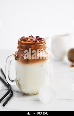 Ice coffee with milk in mason jar and black metal drinking straws on white marble table over white background. Copy space for text. Stock Photo
