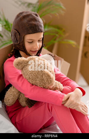 Kid in pink clothes and flight helmet holding teddy bear Stock Photo