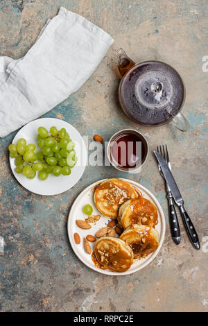 Pancakes with caramel and nuts on white plate with grape and teapot, cup of tea, fork and knife on blue green background Stock Photo
