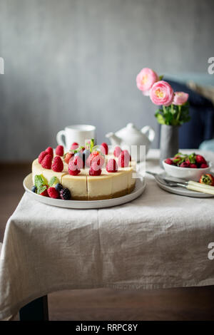 New York cheesecake on table in living room, fork, knife, vase with flowers, teapot and cup near. Concept of healthy live, view of sweet food Stock Photo