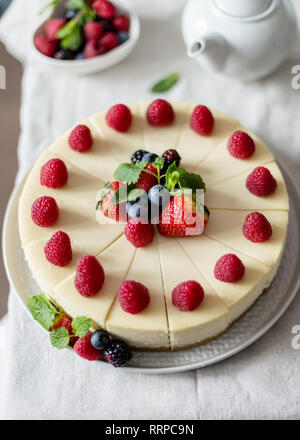 Classic cheesecake with mint, raspberry, blueberry and strawberry on a gray plate on white table. Selective focus, copy space, close up. Concept of fe Stock Photo
