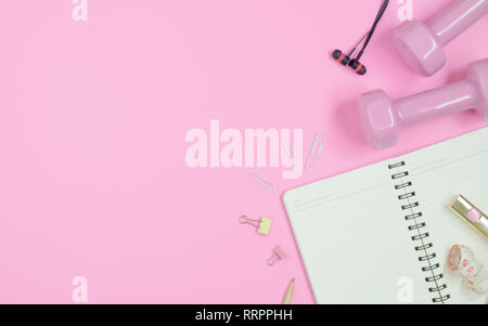Female Fitness, healthy and active lifestyles Concept, dumbbells, blank notebook, tape measure and earphone on pink desktop background. Top view with  Stock Photo