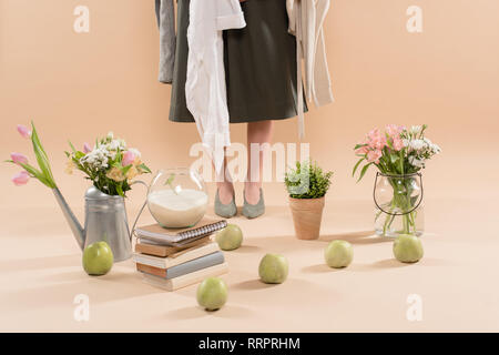 cropped view of woman holding eco clothing near plants and flowers on beige background, environmental saving concept Stock Photo