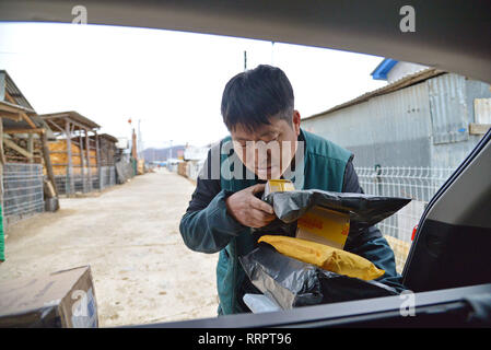 (190226) -- CHANGCHUN, Feb. 26, 2019 (Xinhua) -- Postman Jin Renzhe unloads postal packages in Chunhua Township of Huichun City, northeast China's Jilin Province, Feb. 19, 2019. Jin Renzhe has been working as a postman for 30 years in Chunhua Township, where postal service is inadequate because of steep mountain paths and loosely-scattered villages. Despite that, Jin manages to deliver mails to villagers the same day mails arrive in the town. As many young people work outside the town, Jin bridges them and their parents through delivering packages. Living with eye disease and arthritis, Jin st Stock Photo