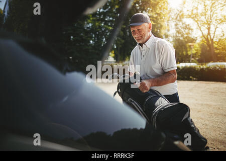 Smiling senior man packing his golf bag into the trunk of his car after playing a round of golf on a sunny afternoon Stock Photo
