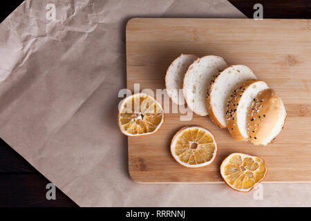 Hot sweet buns cut into pieces on a rustic background. Shaped food with sesame on cutting board and dry oranges. Stock Photo